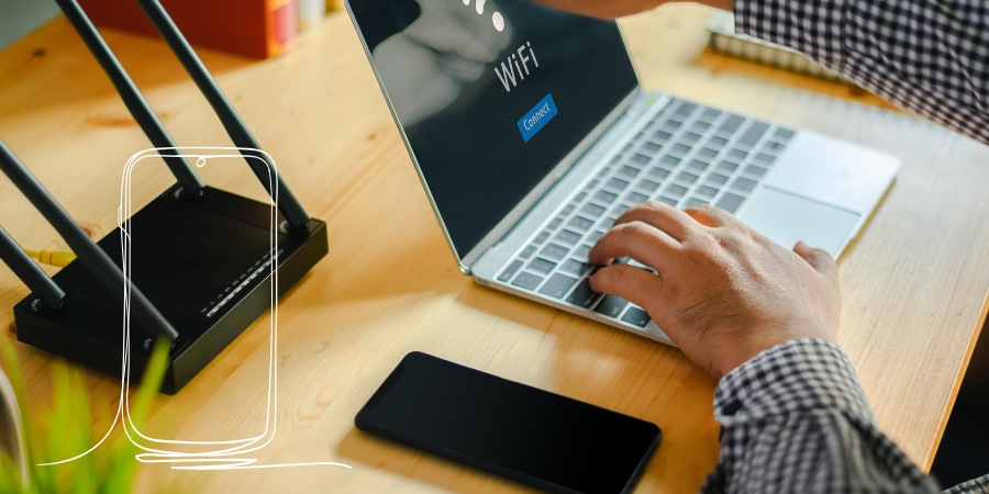 Person connecting a laptop to home WiFi beside a broadband router.